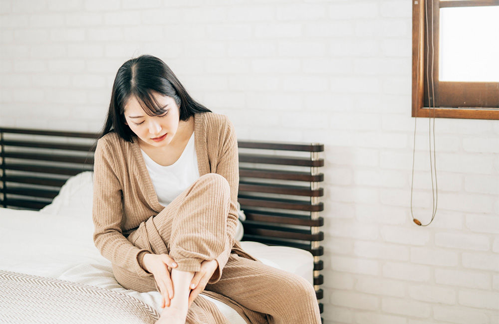ベッドの上で起き上がってパジャマの裾を直す、足元を気にする様子